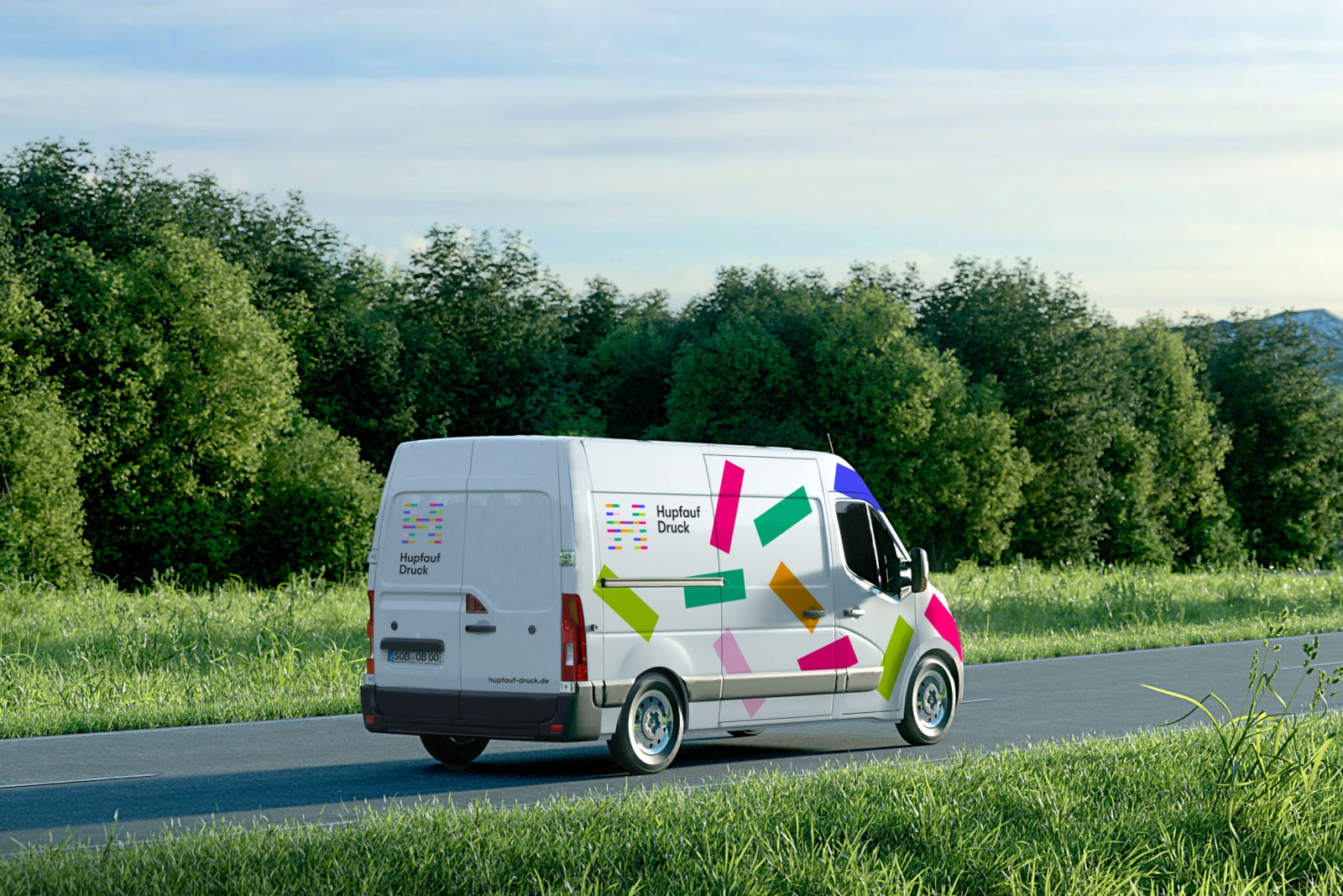 Wei&szlig;er Lieferwagen mit buntem Hupfauf-Druck-Branding auf einer Landstra&szlig;e vor gr&uuml;nen B&auml;umen