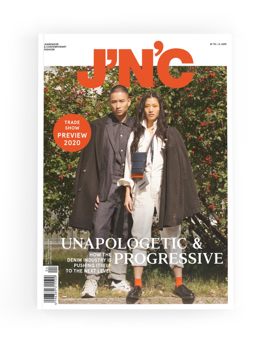 J'N'C Magazine Cover No. 78, Issue 4/2019: Two models wearing dark coats draped over their shoulders and sporting an industrial-style denim look in front of a shrub with red berries; cover story: “Unapologetic & Progressive – How the Denim Industry is Pushing Itself to the Next Level”; with a “Trade Show Preview 2020” button