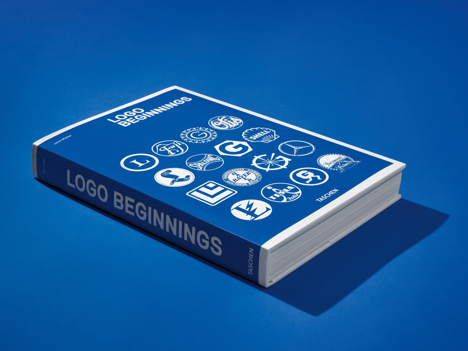 “Logo Beginnings” book mockup photography featuring a preview of historical corporate identity logos on a blue background