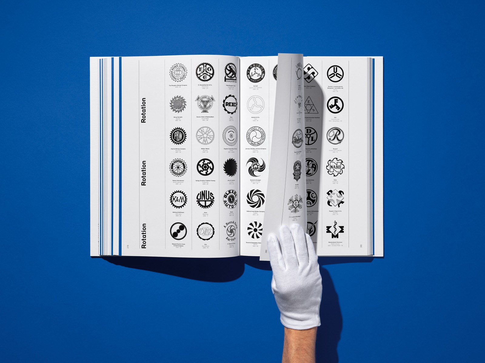 A hand wearing a white glove holds an open page from a book containing an overview of company logos and trademarks in the “Rotation” category