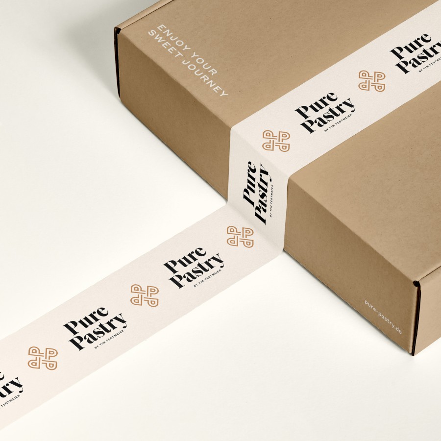 Brown cardboard box featuring Pure Pastry branding: stickers and tape with the logo and lettering in white and copper