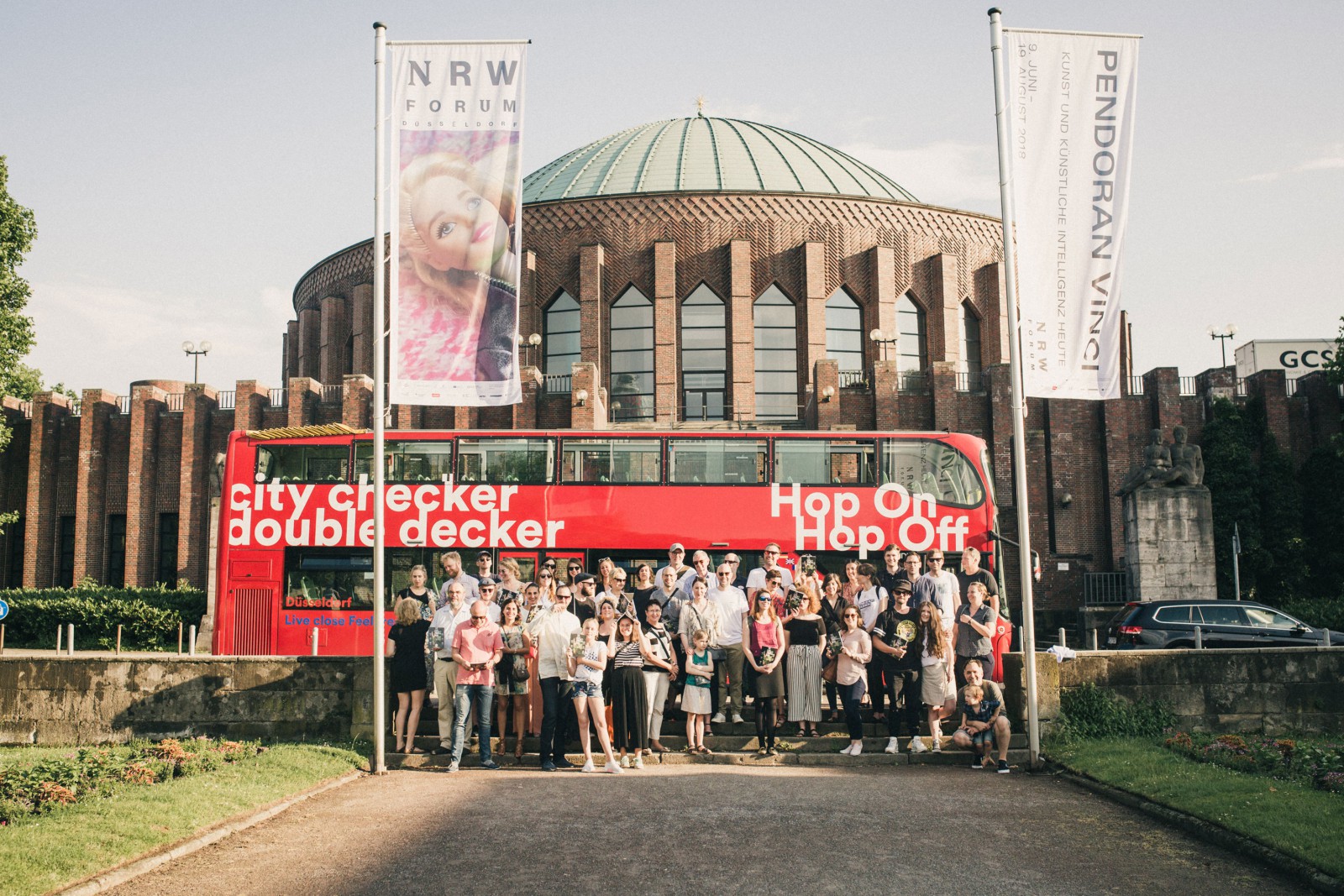 Group in front of the NRW Forum—the Tonhalle in Düsseldorf—with the red double-decker bus “City Checker Double Decker” on the occasion of the release party for THE DORF THE MAG No. 2