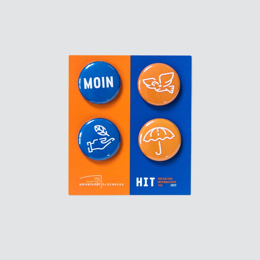 Three round HIT pins in orange and blue: one with the word “MOIN,” one with a stylized bird's wing icon, and one with the HIT logo of the University of Oldenburg