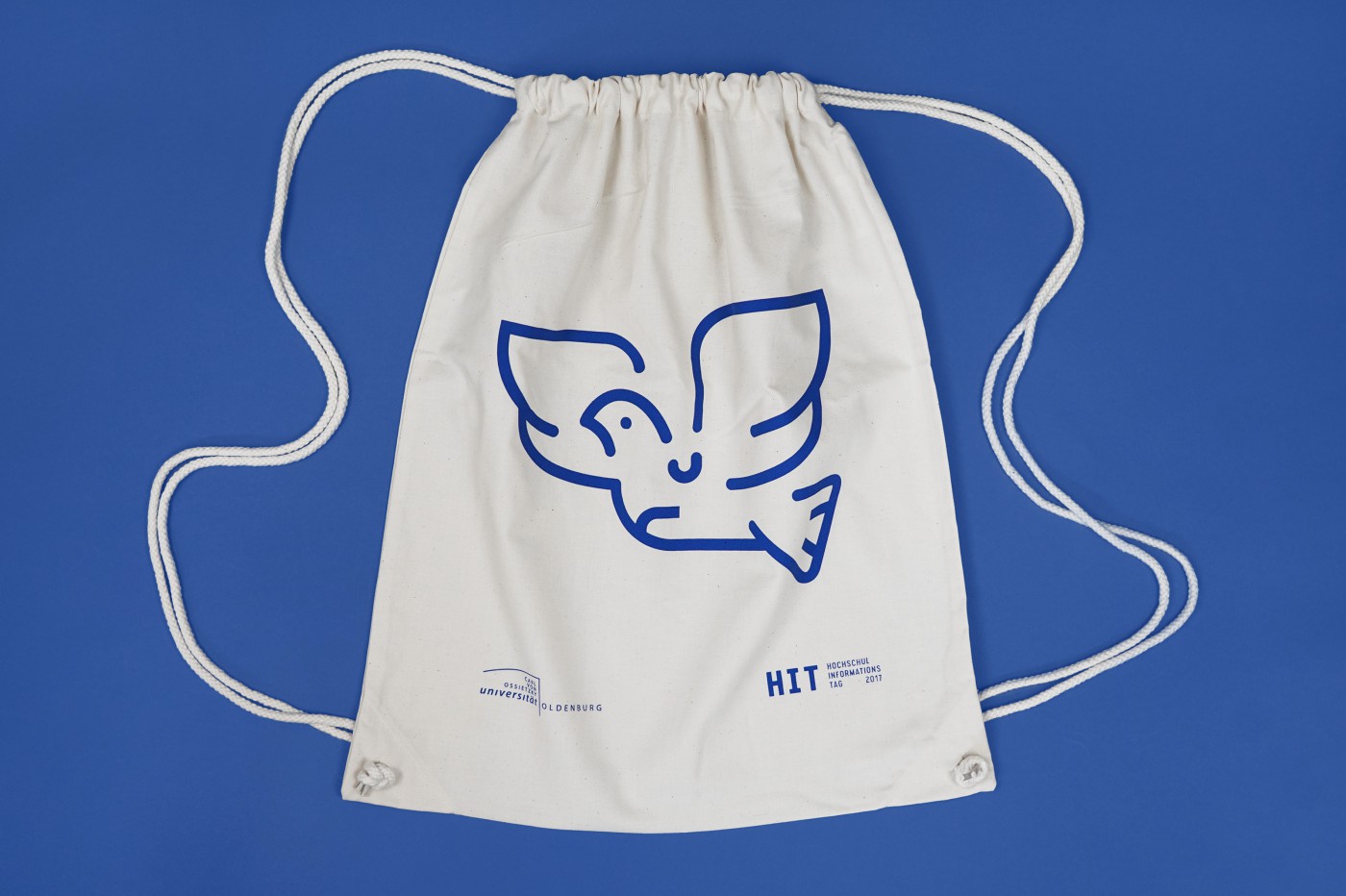 Light-colored cotton gym bag featuring a blue line drawing of a stylized flying bird, a lighthouse, and a bicycle, as well as the logo of Carl von Ossietzky University of Oldenburg and the &ldquo;HIT 2017&rdquo; lettering on a blue background